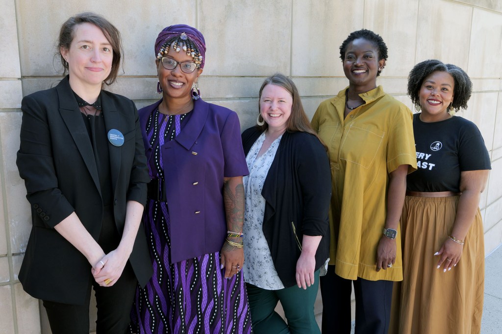 Five women stand together outdoors against a stone wall.