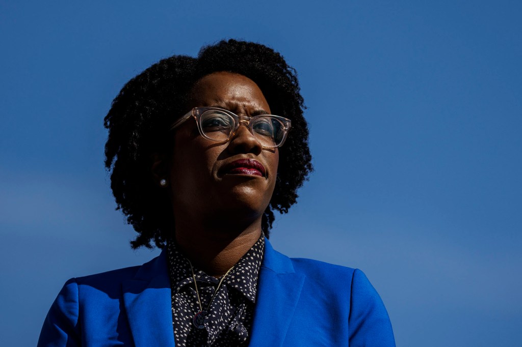 Rep. Lauren Underwood stands outdoors against a blue sky, wearing glasses and a blue blazer.