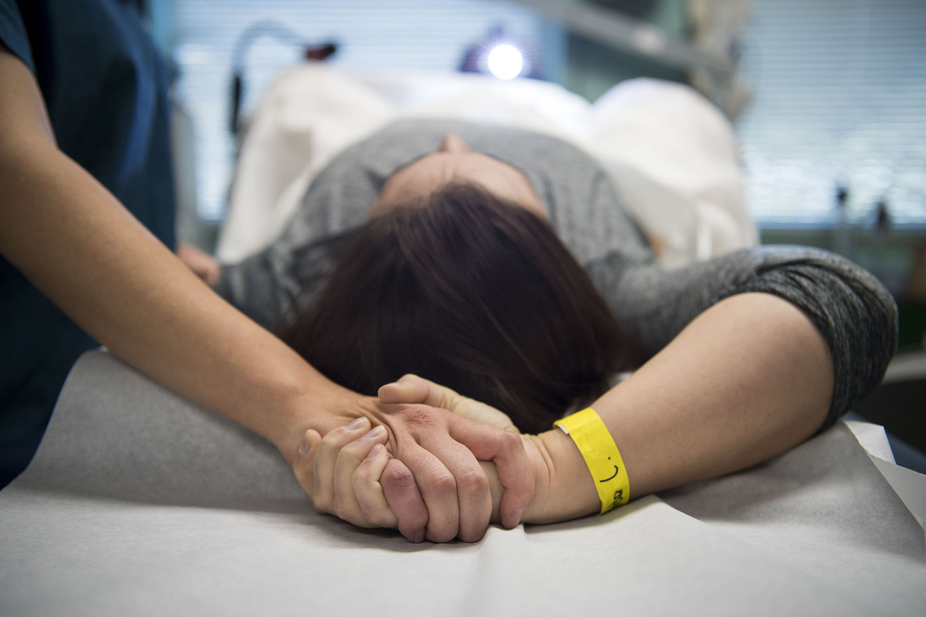A patient lies on an exam table while an doula holds their hand during a procedure at a clinic.