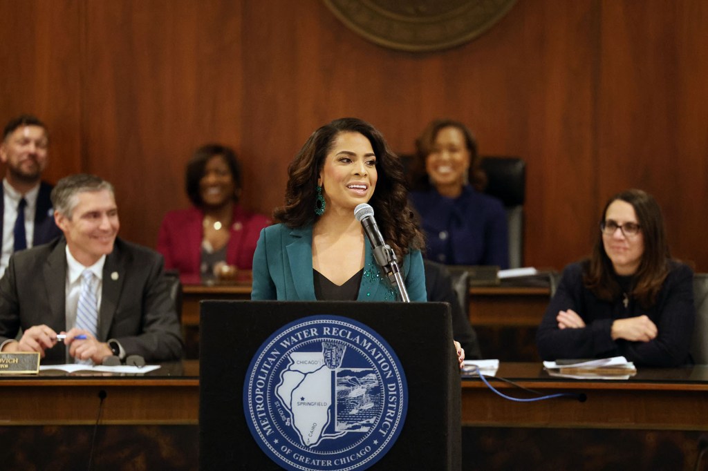 Precious Brady-Davis stands at a podium with the seal of the Metropolitan Water Reclamation District of Greater Chicago, speaking into a microphone during a public meeting.