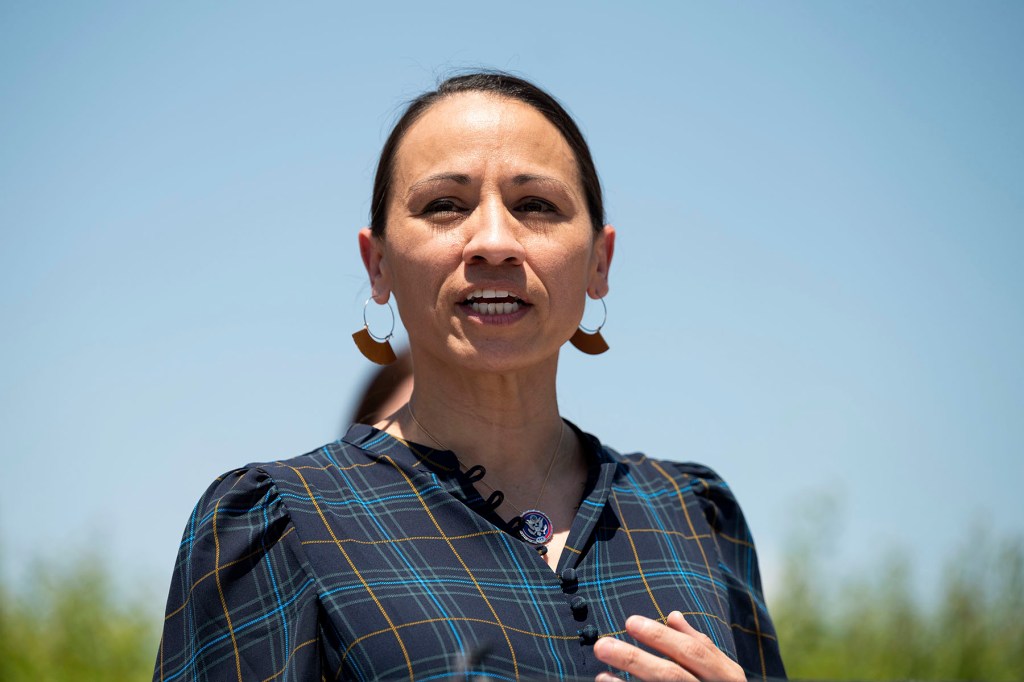 Sharice Davids, in a dark plaid top, speaks outdoors against a blue sky.