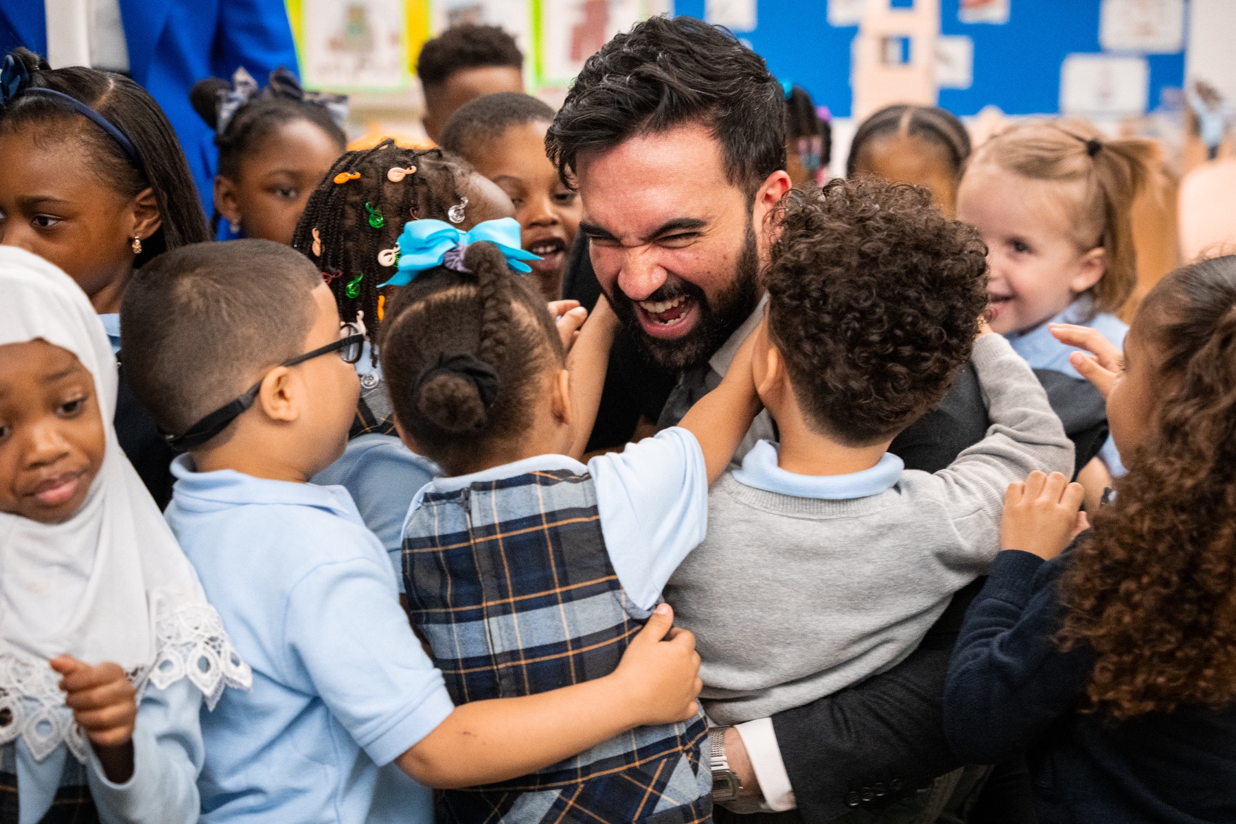 A group of preschoolers in uniforms hug New York Mayor Zohran Mamdani.