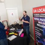 Plumbers union representative talks with a prospective trades student at a booth table