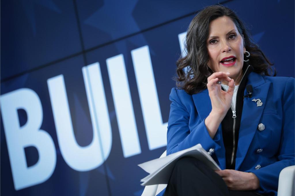 Michigan Gov. Gretchen Whitmer in a blue blazer speaks and gestures while seated before a backdrop reading "BUILD"