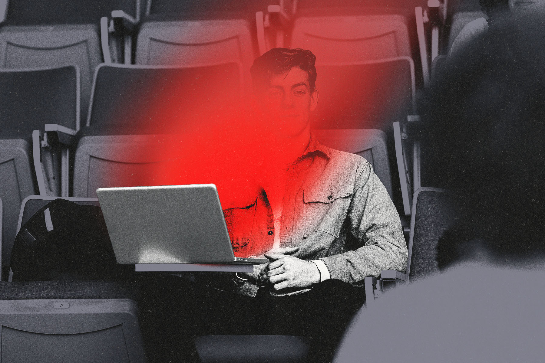 A black and white photo illustration of a male student sitting in auditorium seating with a laptop, partially obscured by a bright red flare across the center of the image coming from his computer screen.