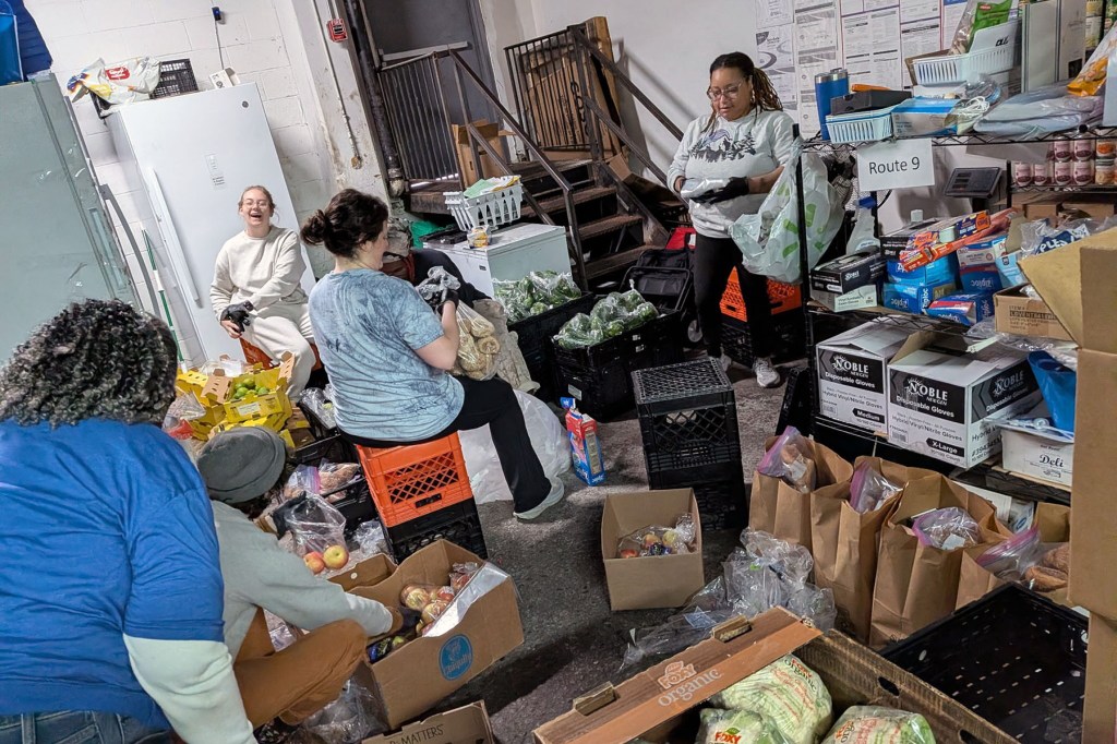 Volunteers sort produce, pantry items and packed grocery bags inside a food distribution warehouse.