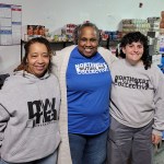 Renee Hill Joyner, Linda James-Rivera and Zoe Ganslaw stand together in front of shelves stocked with food and household supplies.