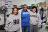 Renee Hill Joyner, Linda James-Rivera and Zoe Ganslaw stand together in front of shelves stocked with food and household supplies.