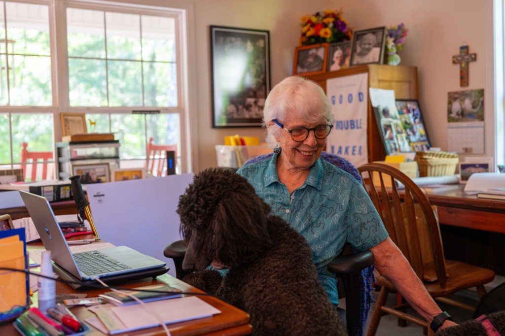 Rev. Heyward Carter sits at a desk on her computer with a dog.