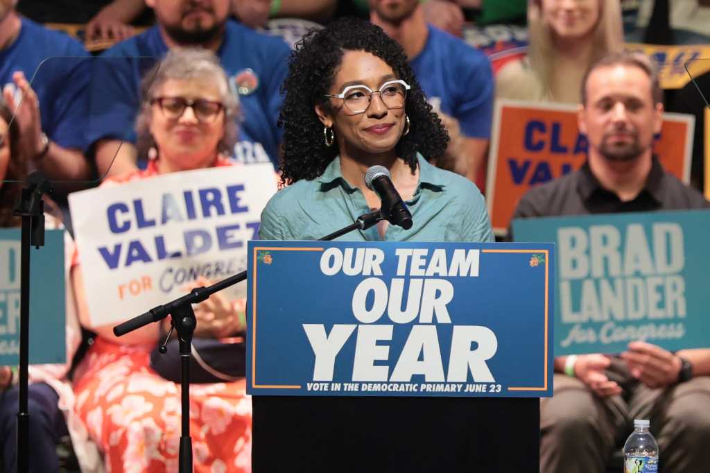 Darializa Avila Chevalier speaks at a rally with a crowd behind her and a sign on the lectern that says "Our Team Our Year"