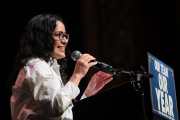Claire Valdez speaks into a microphone; to the side is a sign that says 