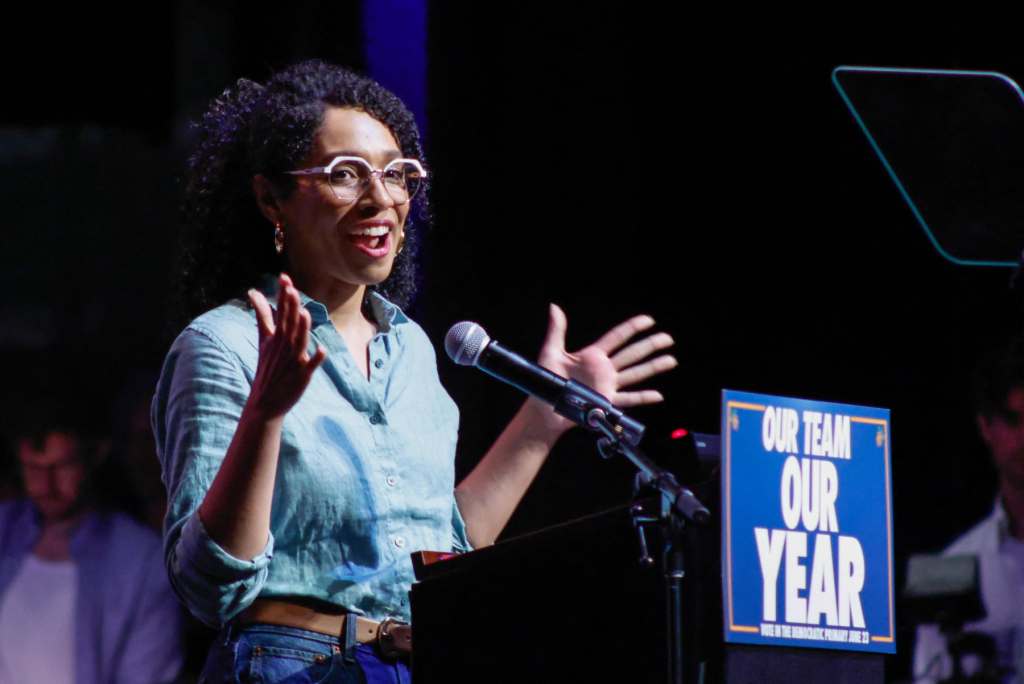 Darializa Avila Chevalier speaks into a microphone with a sign on it that says Our Team Our Year