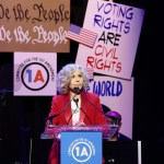 Jane Fonda, in a red suit, speaks onstage.
