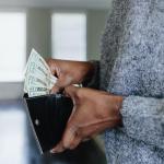 A close-up image of a woman's hands inserting twenty dollar bills into her wallet.