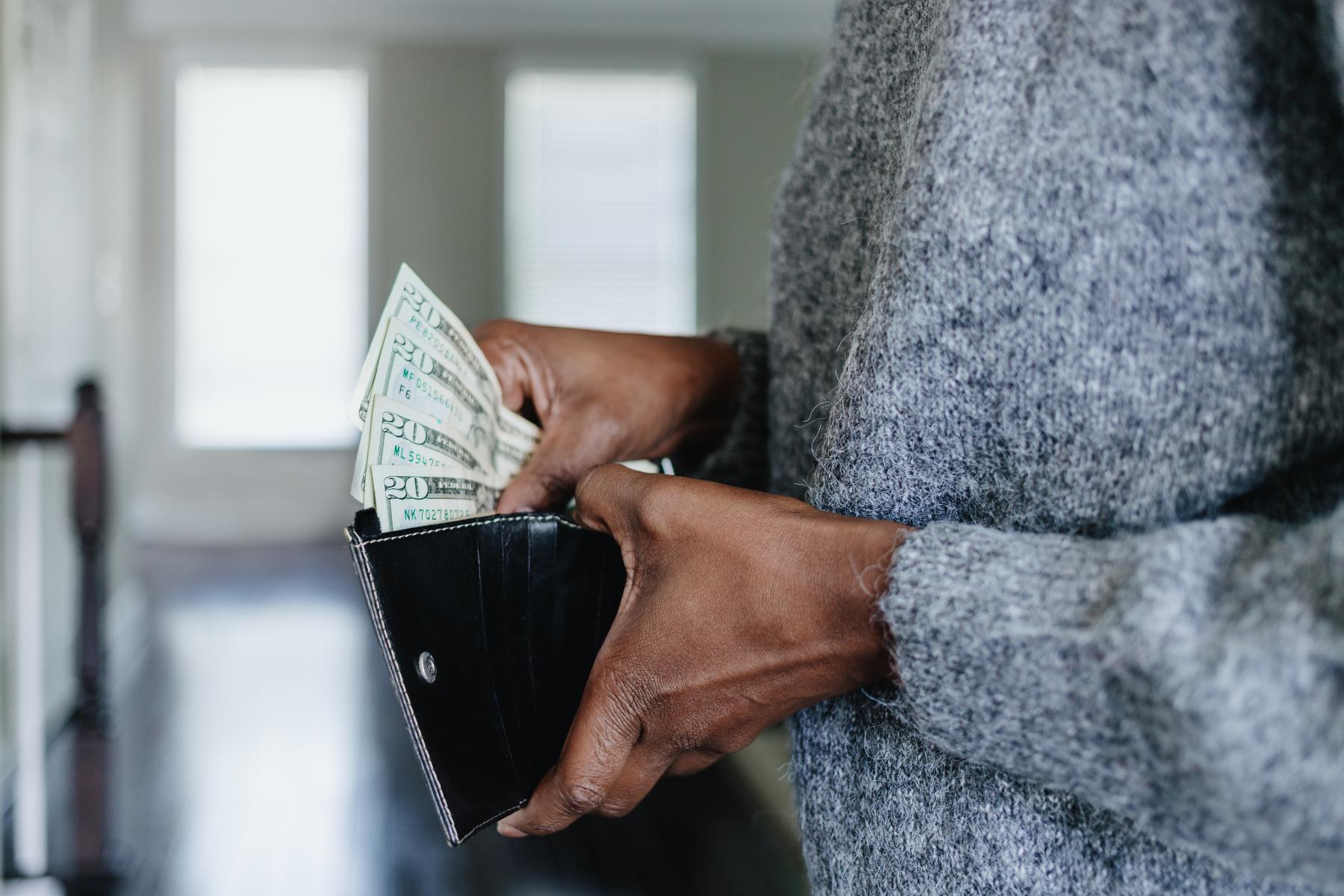 A close-up image of a woman's hands inserting twenty dollar bills into her wallet.