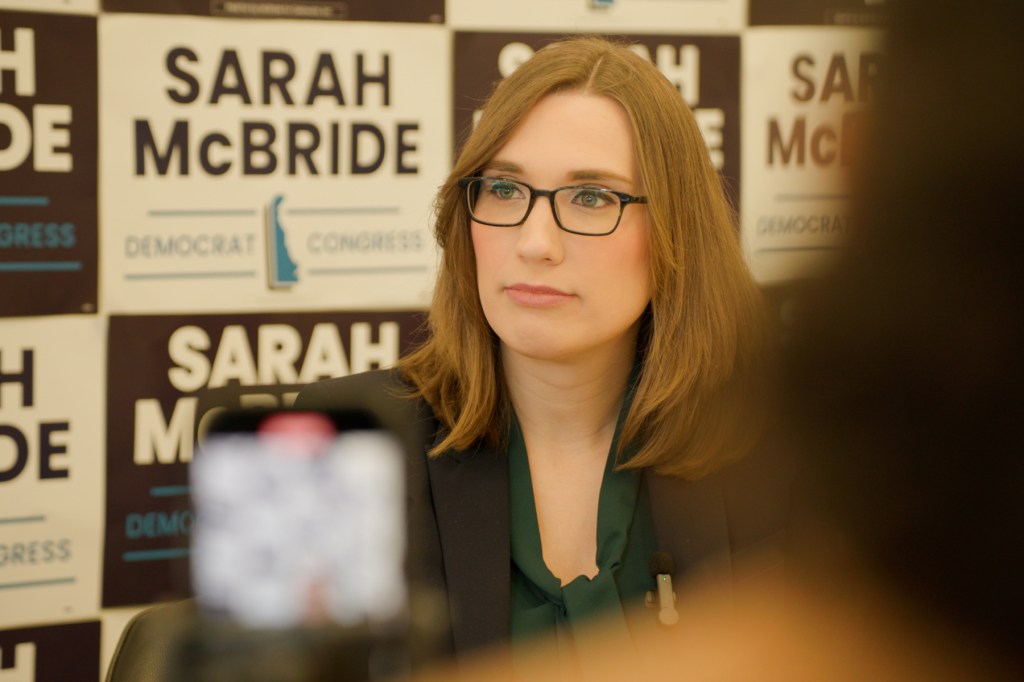 Sarah McBride sits with campaign posters behind her.