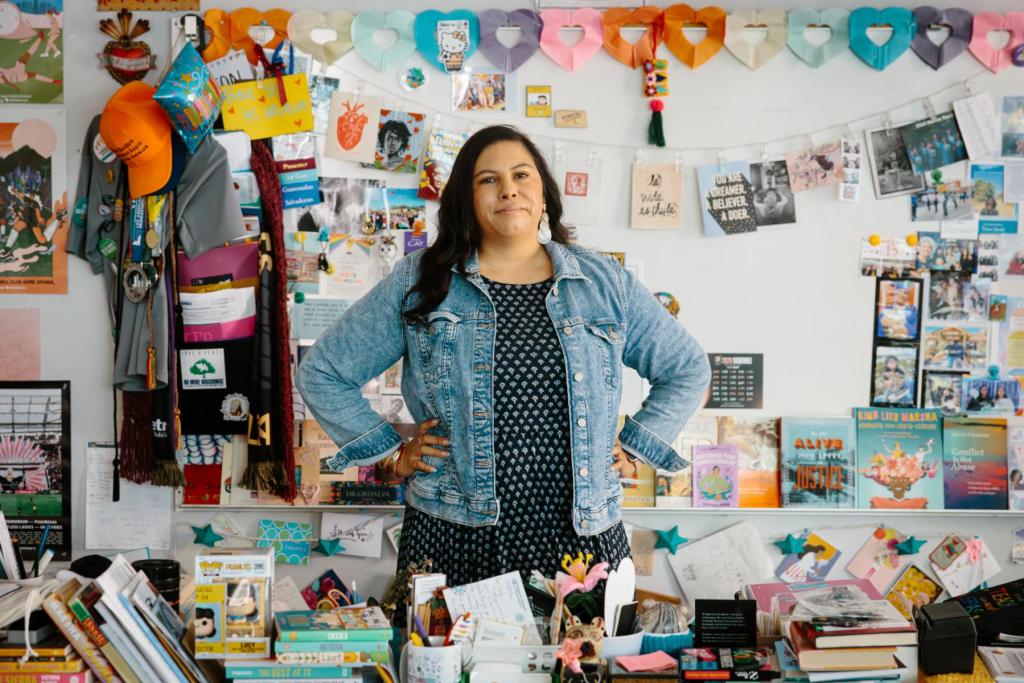 A woman stands behind a desk in a classroom lined with colorful art.