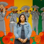 A woman stands in front of a colorful mural celebrating Mariachi Arcoíris de Los Angeles.