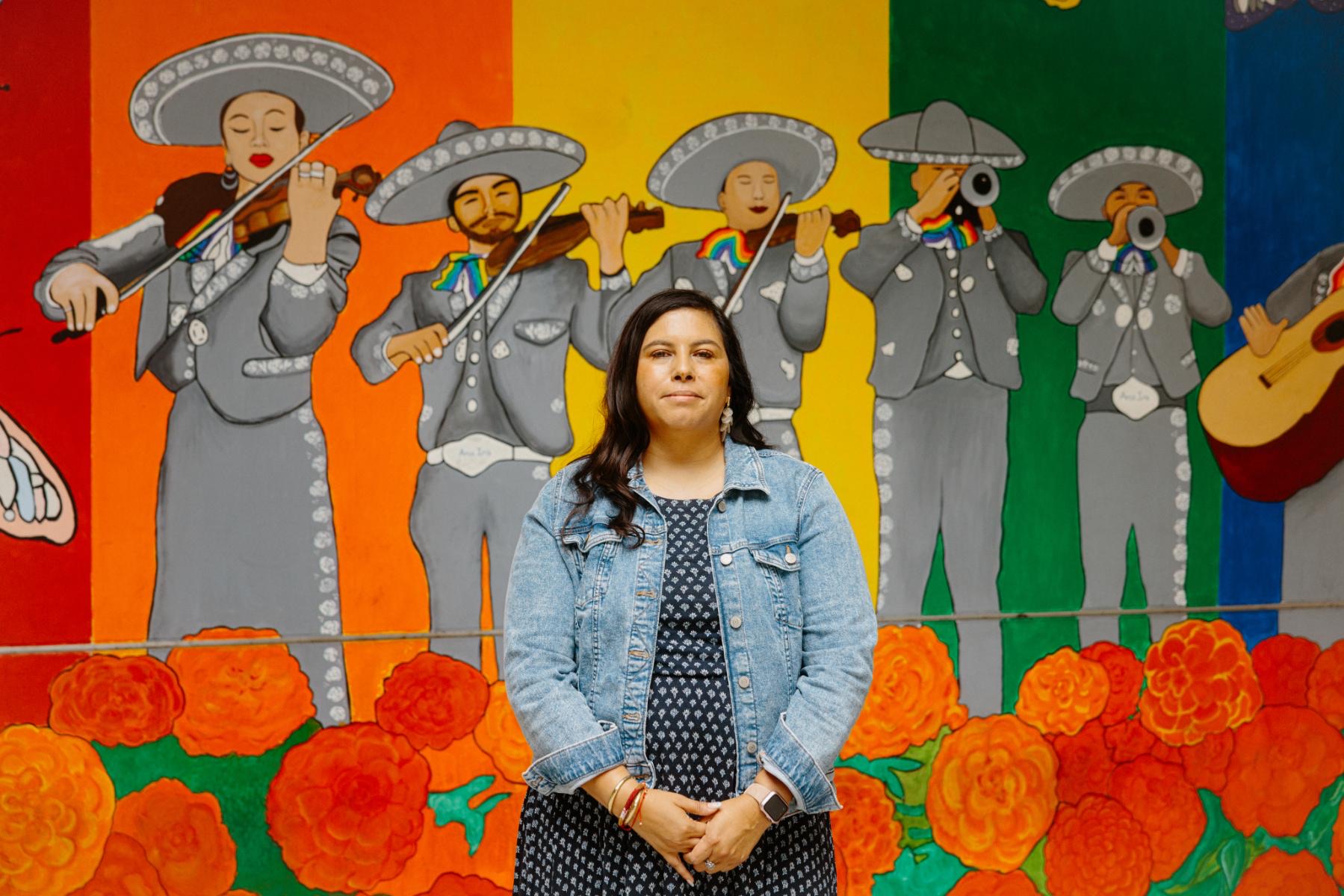 A woman stands in front of a colorful mural celebrating Mariachi Arcoíris de Los Angeles.