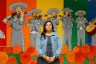 A woman stands in front of a colorful mural celebrating Mariachi Arcoíris de Los Angeles.