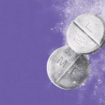Two mifepristone pills appear submerged in water on a purple background.