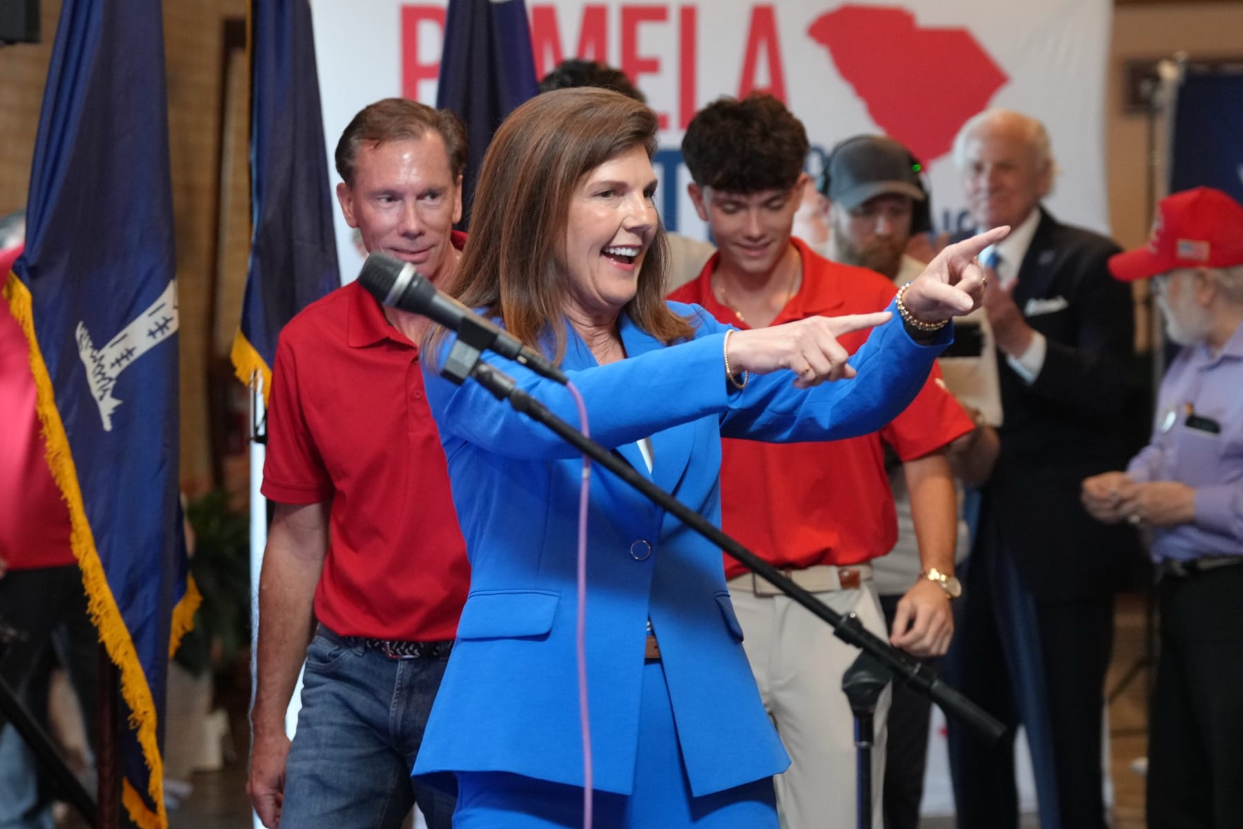 Pamela Evette, in a blue suit, points while standing in front of a crowd at a rally