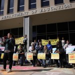 Demonstrators protest with signs outside of the U.S. Department of Education.