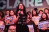 Claire Valdez speaks with a crowd behind her holding signs that says Housing for All and Abolish ICE