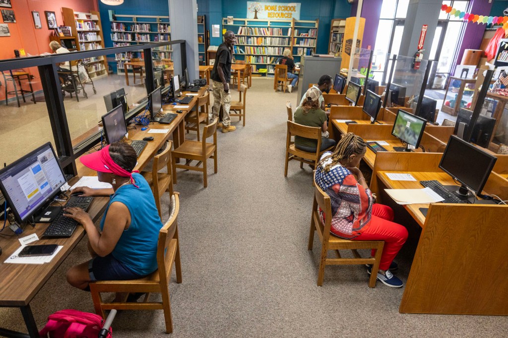 People use desktop computers and browse shelves inside a public library.