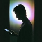 A person looks at their phone with a light behind their head silhouetting them.