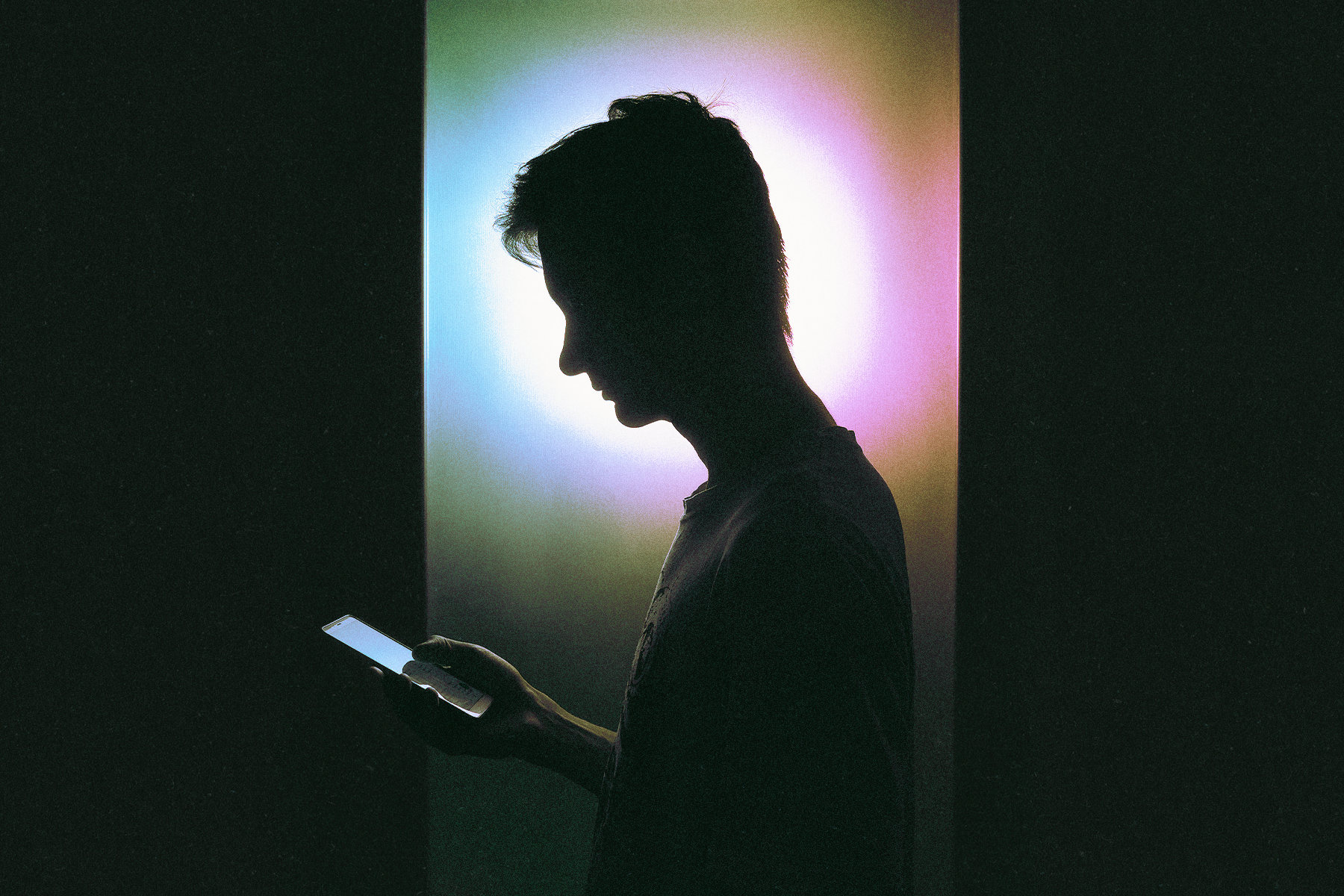 A person looks at their phone with a light behind their head silhouetting them.