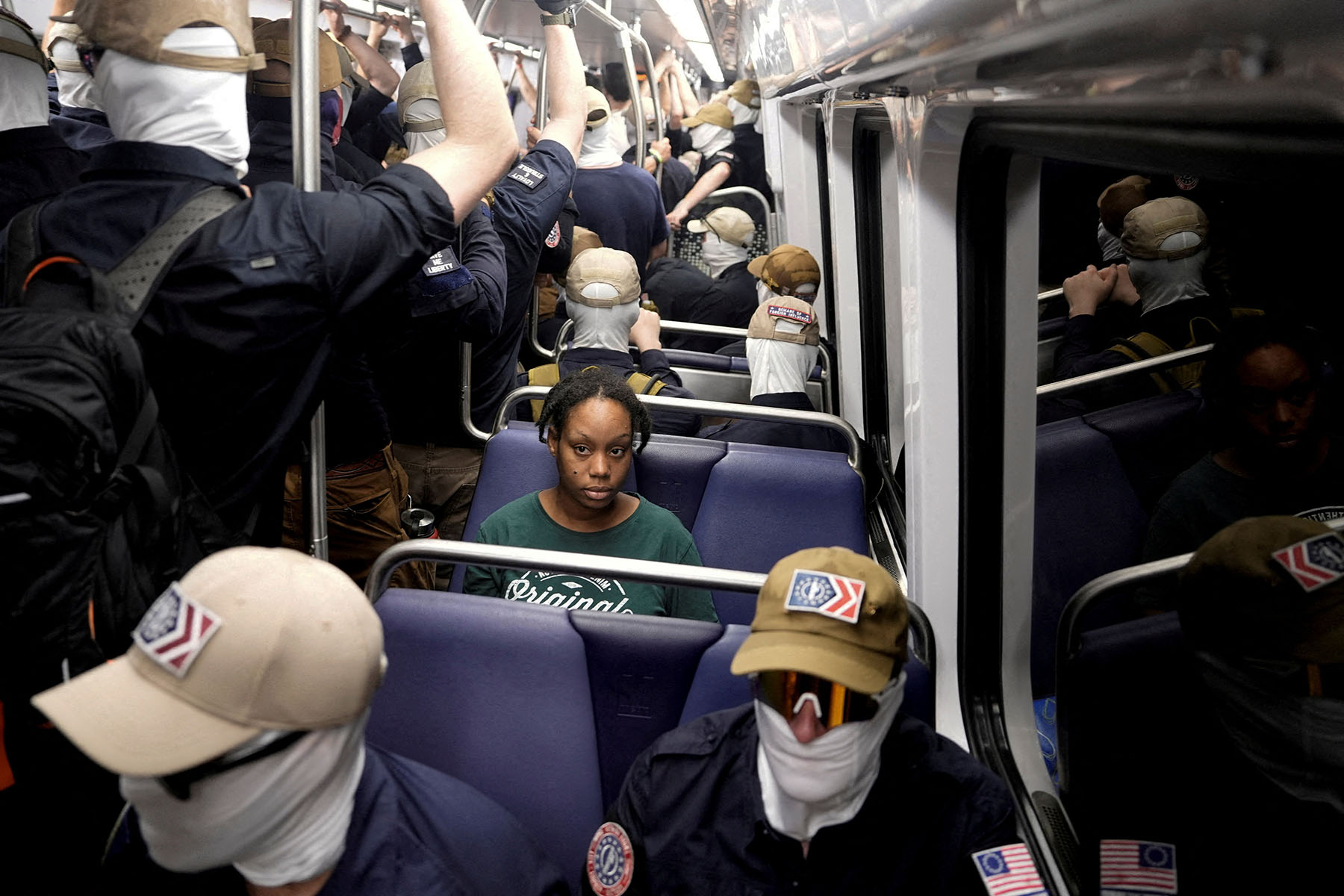 A commuter looks on as masked members of the White nationalist group Patriot Front ride the metro on the 250th anniversary of independence.