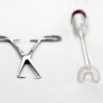 A metal tenaculum and a white suction-based gynecological device sit side by side on a white surface.