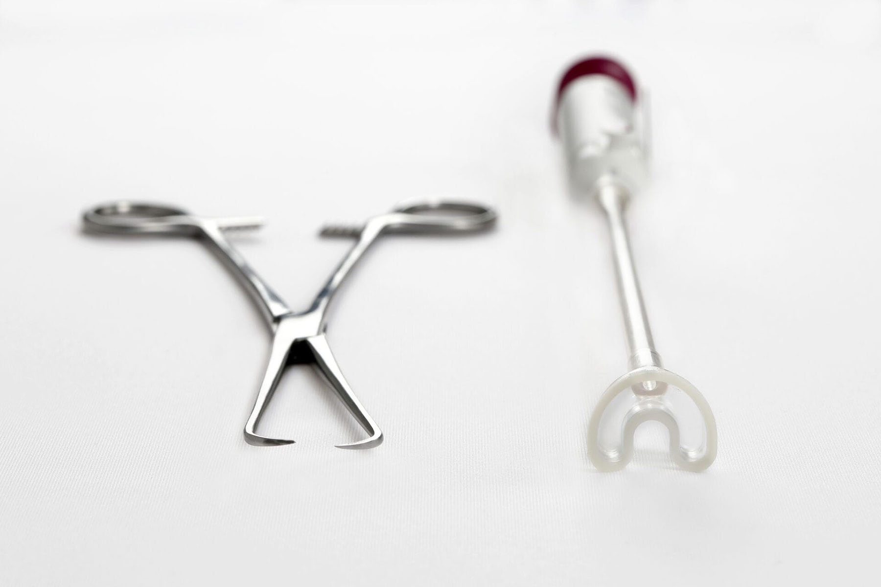 A metal tenaculum and a white suction-based gynecological device sit side by side on a white surface.