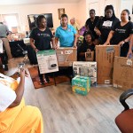 Volunteers and community members gather around donated baby supplies, including diapers, a high chair, a fan and a bottle warmer.