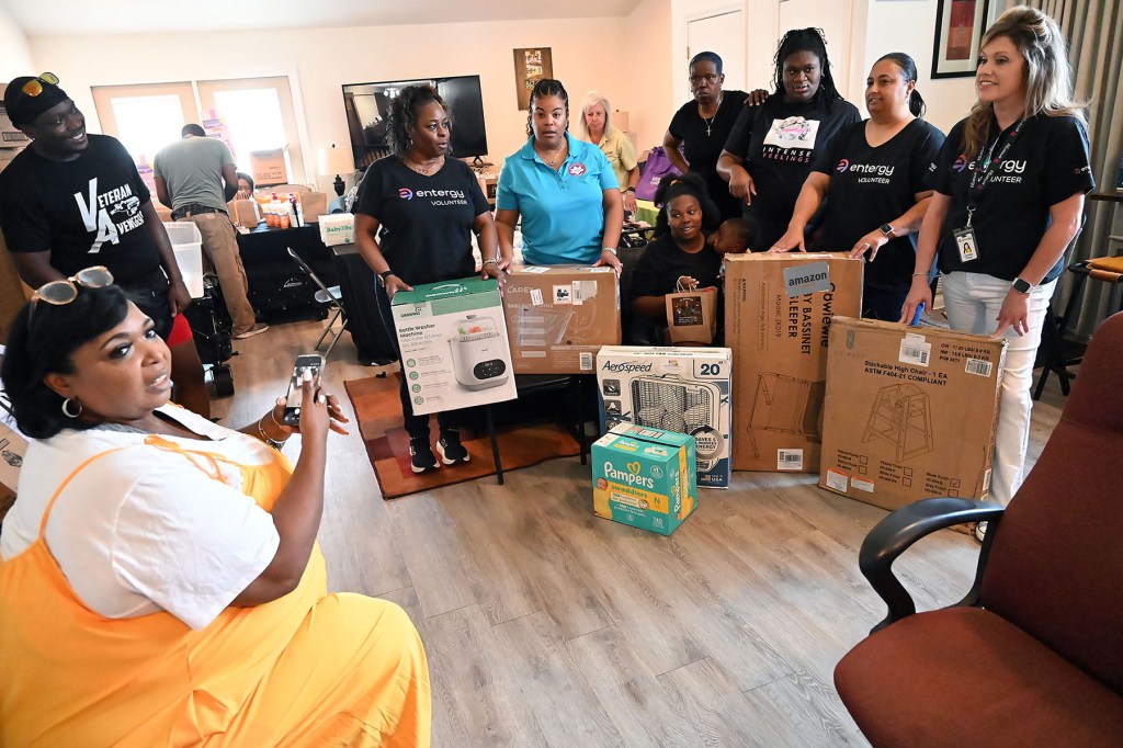 Volunteers and community members gather around donated baby supplies, including diapers, a high chair, a fan and a bottle warmer.