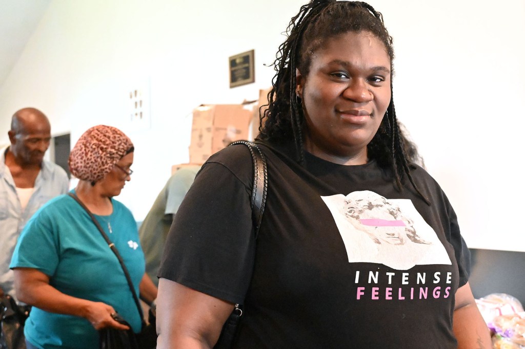 A woman wearing a black T-shirt smiles, at a community distribution event.
