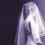 A young girl wearing a veil and a white dress stands against a dark purple background.