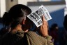 A demonstrator holds a protest flyer over their face to block the sun. The flyer reads “Stop ICE Terror!” and calls for justice for Lorenzo and Joan and the jailing of ICE agents.