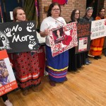 A line of people stand holding signs about missing and murdered Indigenous women.