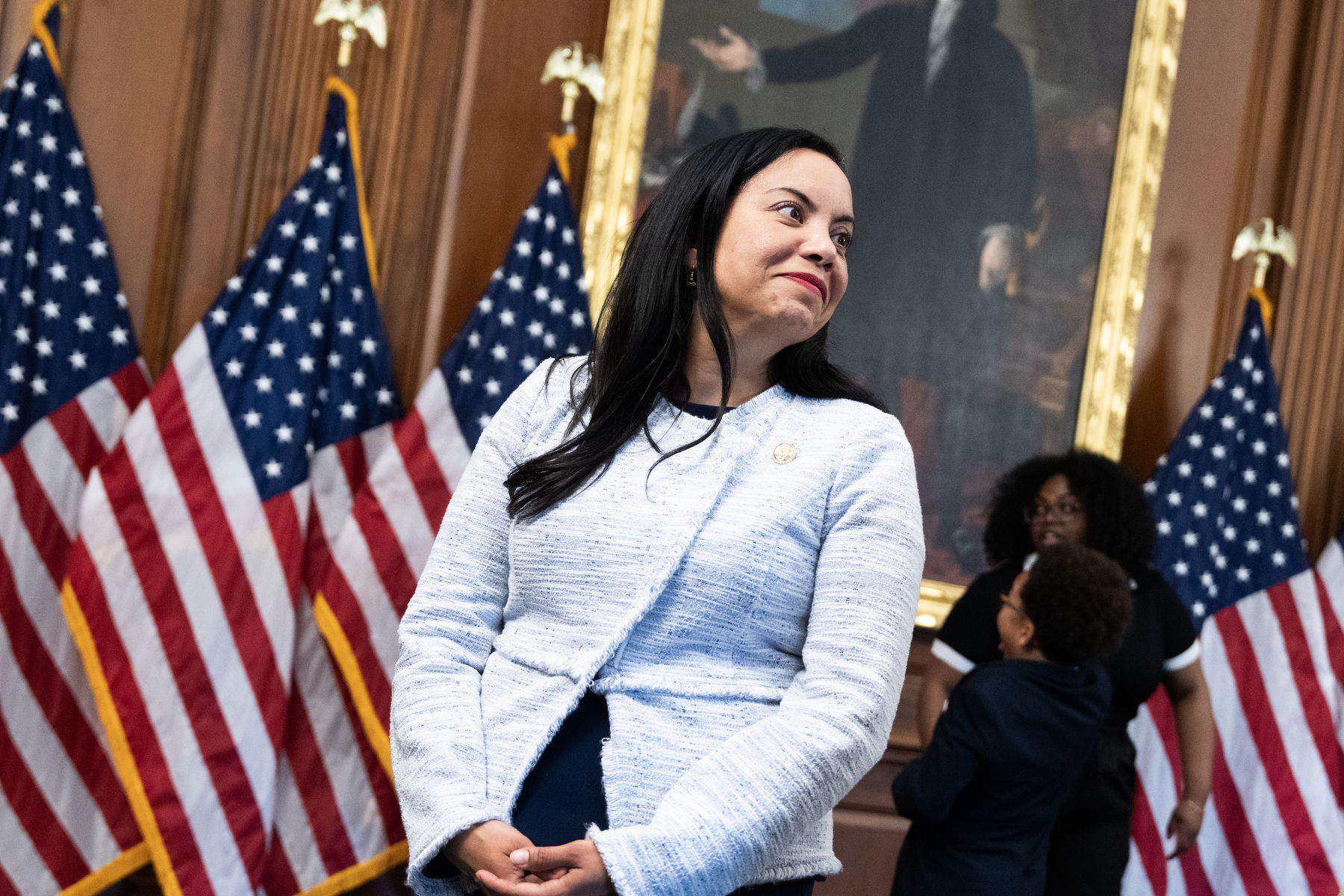 Mejia smiles while looking off-camera in between United States flags.