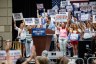 Senate candidate Abdul El-Sayed smiles at a podium as supporters behind him raise campaign signs.