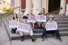 Five young people sit on the steps of a building, each holding signs that read, “No hate in WA state. Vote No on I-001 & I-638.”