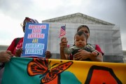A woman holds her baby and an America flag in front of the Supreme Court alongside someone holding a sign saying American Born Children are American Children.
