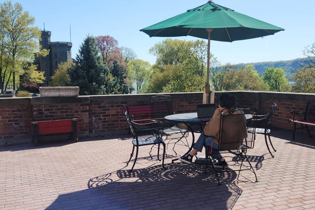 A person sits at a table with an umbrella on a brick patio, their back to the camera.