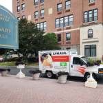 A U-haul truck is parked in front of a brick building with a sign saying Rosary Hall.