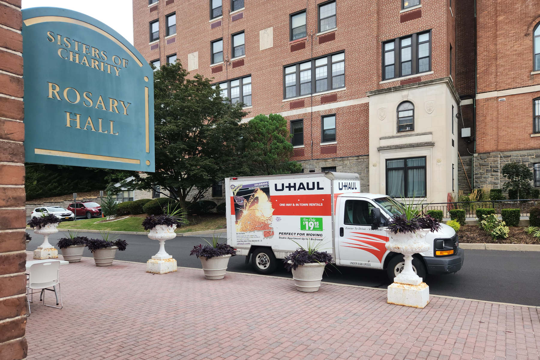 A U-haul truck is parked in front of a brick building with a sign saying Rosary Hall.