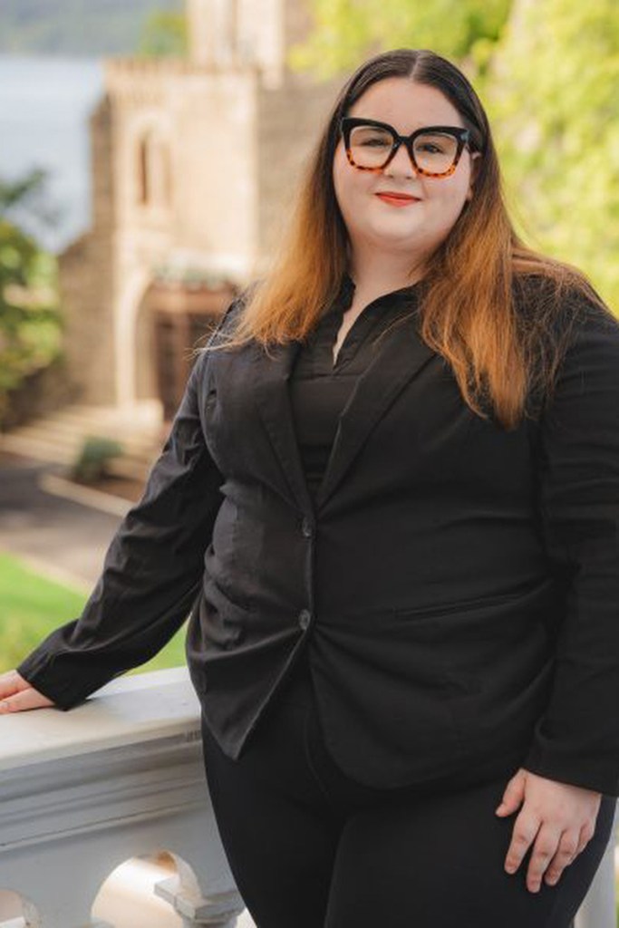 A portrait of a woman in a black suit, standing and looking into the camera.