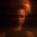 A softly lit blurred portrait of a woman looking toward the camera.