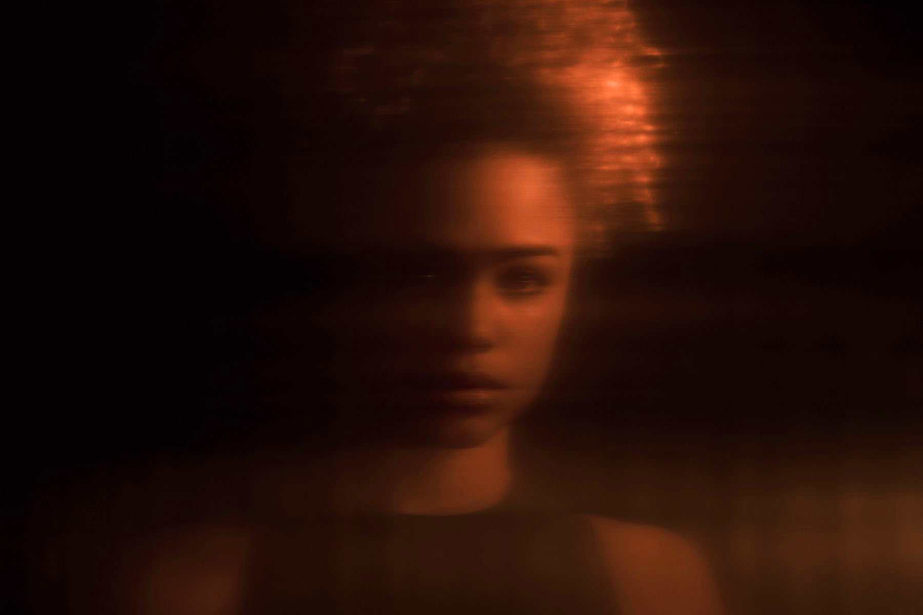 A softly lit blurred portrait of a woman looking toward the camera.